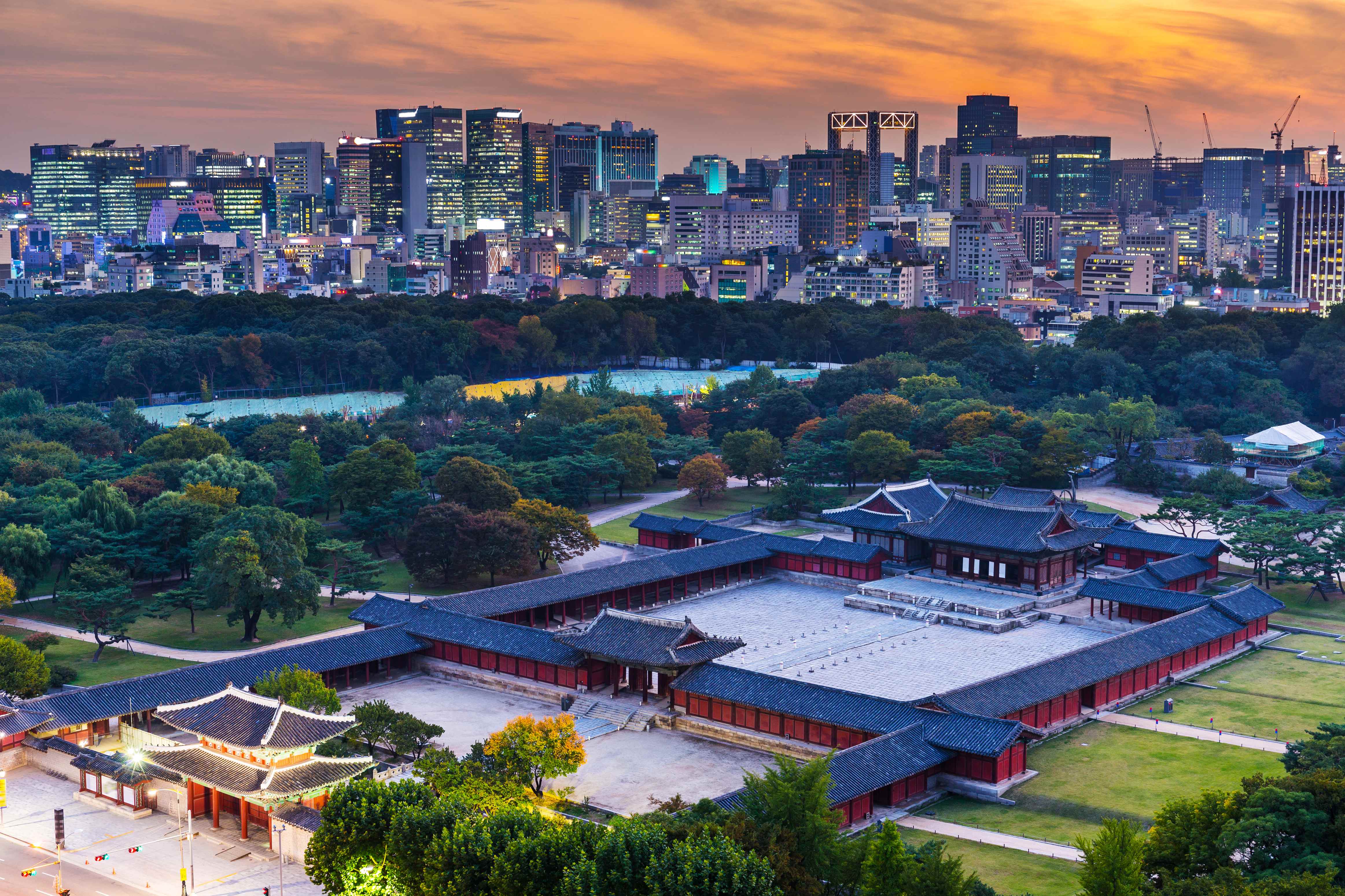 Aerial view of a traditional Korean palace with the Seoul skyline at sunset